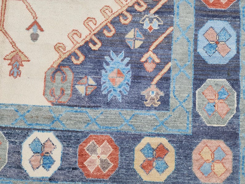 May include: Close-up of a blue and cream rug with a geometric pattern. The rug has a border of blue and cream, and the center is filled with a repeating pattern of flowers and leaves.
