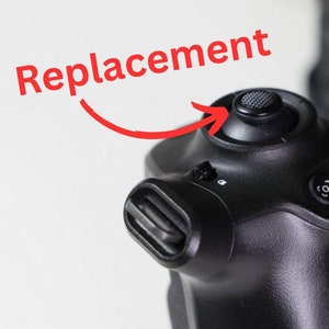 Puede incluir: Primer plano de un panel de control de cámara negro con un botón texturizado que indica "Reemplazo" en rojo. El panel presenta botones adicionales etiquetados como "EXP" y un símbolo. La imagen destaca una pieza de repuesto para una cámara.