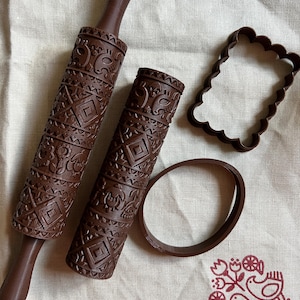 May include: A set of brown baking tools, including a patterned rolling pin, a smaller patterned roller, a scalloped-edge cookie cutter, and a round ring. The rolling pin and roller feature repeating geometric and floral designs.