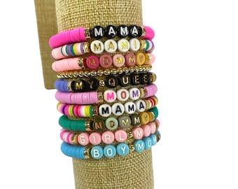 May include: A stack of colorful beaded bracelets with different words spelled out on them, including "Mama", "Mommy", "My Queen", "Mom", "Girl Mom", and "Boy Mom".
