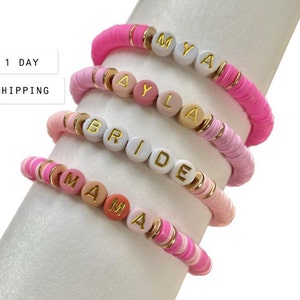 May include: Four pink, white and peach beaded bracelets with gold letter beads spelling out the names "MYA", "AYLA", "BRIDE", and "MAMA".