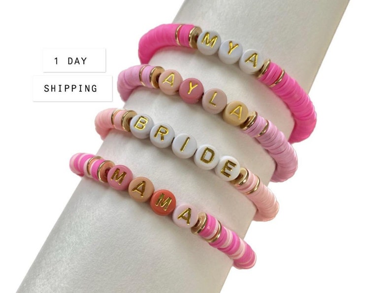May include: Four pink, white, and peach beaded bracelets with gold letter beads spelling out the names "MYA", "AYLA", "BRIDE", and "MAMA".