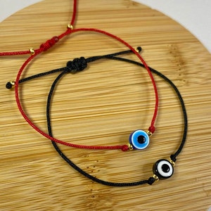 May include: Two adjustable bracelets with evil eye charms. One bracelet is red string with a blue evil eye charm and the other is black string with a black and white evil eye charm.