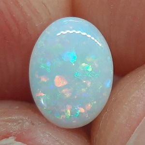 May include: A white oval opal gemstone with iridescent blue, green, and orange flashes.
