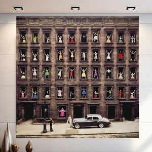 May include: A black and white photograph of a building with windows. People are standing in the windows, and a black car is parked in front of the building.