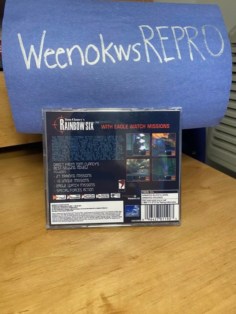 May include: Back of a Tom Clancy's Rainbow Six video game case with a blue background. The game features Eagle Watch missions and special forces action. The case is rated Teen 13+ for animated blood and gore and animated violence.