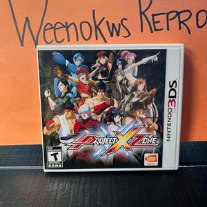 May include: A Nintendo 3DS game case for Project X Zone. The cover art features a group of anime-style characters in various action poses. The game case is white with the Nintendo 3DS logo on the side. The game is rated T for Teen.