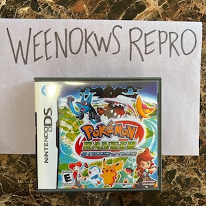 Op de afbeelding: Een Nintendo DS-spelcartridge voor Pokémon Ranger: Schaduwen van Almia. De spelverpakking is zwart met een kleurrijk beeld van Pokémon-personages op de voorkant. De ESRB-classificatie "E" voor iedereen is zichtbaar in de linkerbenedenhoek.