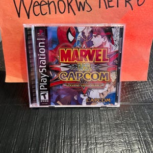 May include: A PlayStation game case for "Marvel vs. Capcom: Clash of Super Heroes." The cover features Spider-Man and other characters in a colorful, action-packed design. The game is rated "T" for Teen.