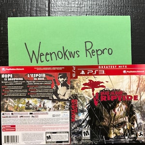 May include: A PlayStation 3 video game case for Dead Island Riptide Greatest Hits. The front cover features a dark, graphic illustration of a zombie head with a red palm tree silhouette. The back cover includes game details and text in English and French.