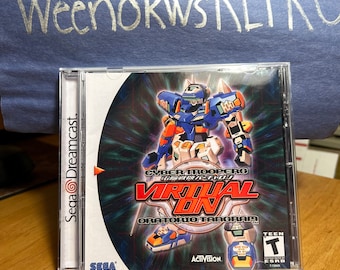 May include: A Sega Dreamcast game case for "Cyber Troopers Virtual-On: Oratorio Tangram." The cover art features a blue, orange, and white robot. The game case is in a clear plastic case with the Sega Dreamcast logo on the spine.