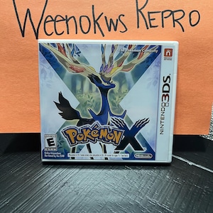 May include: A white Nintendo 3DS game case with a blue and black Pokemon X logo. The game features a blue and black Pokemon character with a large, branching head. The text "The Pokemon Company" and "Nintendo" are visible on the case.