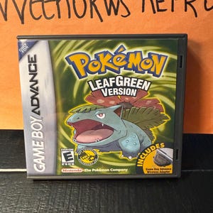 May include: A Game Boy Advance cartridge for Pokémon LeafGreen Version. The game case is black with the game title in yellow and green. The cover art features a green and blue Pokémon character. Includes a Game Boy Advance Wireless Adapter.