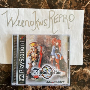Może przedstawiać: Pudełko gry PlayStation dla Threads of Fate, gry RPG na konsolę PlayStation. Pudełko jest czarne z srebrnym logo PlayStation i niebiesko-białą etykietą klasyfikacji ESRB. Okładka gry przedstawia kolorową ilustrację dwóch postaci, mężczyzny i kobiety, stojących przed kamienną ścianą. Tytuł gry to "Threads of Fate", a deweloperem jest SquareSoft.