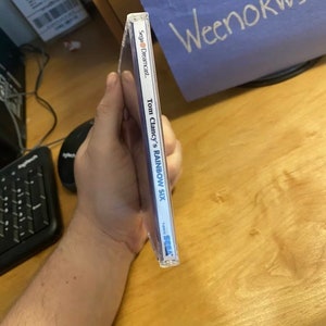 May include: A Sega Dreamcast game case for Tom Clancy's Rainbow Six. The case is blue and white with the game title and Sega Dreamcast logo.