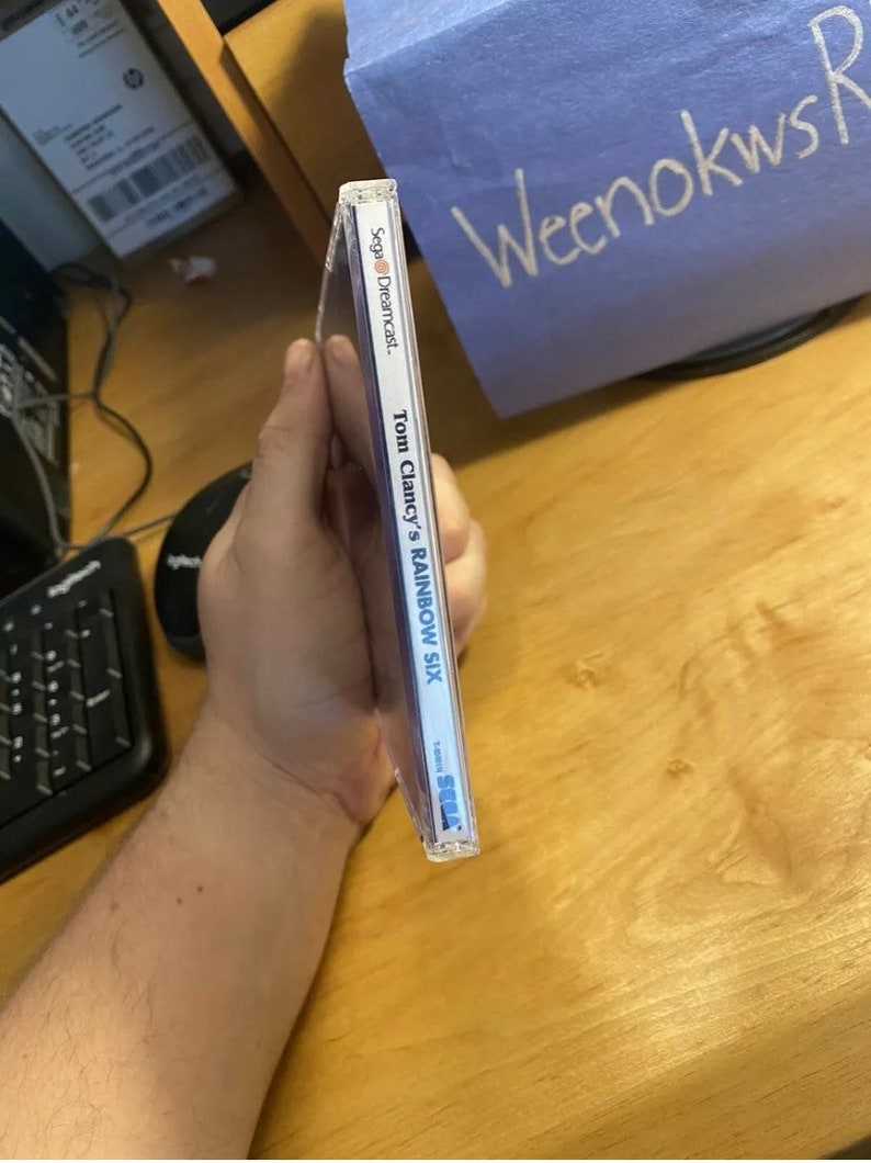 May include: A Sega Dreamcast game case for Tom Clancy's Rainbow Six. The case is blue and white with the game title and Sega Dreamcast logo.