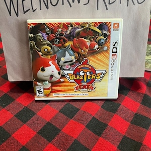 Op de afbeelding: Een Nintendo 3DS-spelcartridge voor Yo-kai Watch Blasters: Red Cat Corps. Het spel heeft een rood, wit en blauw kattenpersonage op de voorkant van de cartridge.