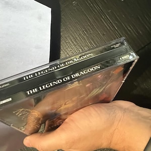 K&ouml;nnte beinhalten: Zwei schwarze PlayStation-Spieleboxen, die &uuml;bereinander gestapelt sind. Die obere Box hat den Text "The Legend of Dragoon" aufgedruckt. Die untere Box hat den Text "The Legend of Dragoon" aufgedruckt. Die untere Box hat auch den Text "4 Discs" aufgedruckt.