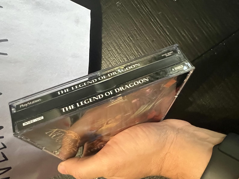 K&ouml;nnte beinhalten: Zwei schwarze PlayStation-Spieleboxen, die &uuml;bereinander gestapelt sind. Die obere Box hat den Text "The Legend of Dragoon" aufgedruckt. Die untere Box hat den Text "The Legend of Dragoon" aufgedruckt. Die untere Box hat auch den Text "4 Discs" aufgedruckt.