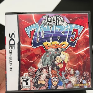 May include: A Nintendo DS game case for "Little Red Riding Hood's Zombie BBQ." The cover features a vibrant design with the title in large, stylized letters. The artwork includes zombie characters and a red and purple background.