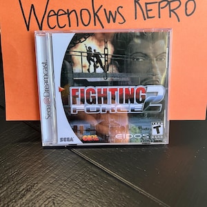May include: A Sega Dreamcast game case for Fighting Force 2. The case is black with a silver spine. The game title is in white with a red 2. The ESRB rating is Teen.