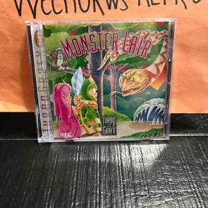 May include: A TurboGrafx-16 video game case for "Monster Lair." The cover art shows a cartoon illustration of a warrior with a sword facing a snake. The game title is in a pink and white font. The case is in a clear plastic case.