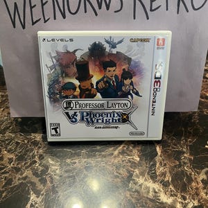 May include: A Nintendo 3DS game cartridge for Professor Layton vs Phoenix Wright: Ace Attorney. The game features a cartoon illustration of the characters Professor Layton and Phoenix Wright.