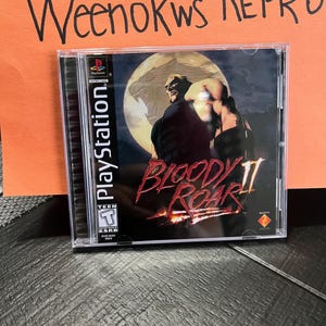 Op de afbeelding: Een PlayStation-gamecase voor Bloody Roar II. De case is zwart met een rood en wit ontwerp. De game toont een weerwolf-personage met een rode achtergrond.