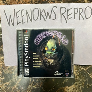 Puede incluir: Una caja de juego de PlayStation para Oddworld: Abe's Odyssey. La caja es negra con un personaje alienígena verde en la parte delantera. El juego está clasificado como "KA" para niños y adultos por la ESRB.
