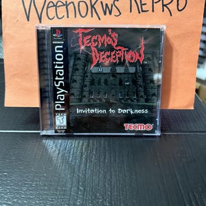 Puede incluir: Caja de juego de PlayStation para "Tecmo's Deception: Invitation to Darkness". La portada presenta un castillo oscuro con un título rojo. La caja del juego está en una funda de plástico transparente con el logotipo de PlayStation.
