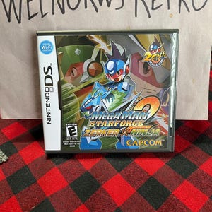 May include: A Nintendo DS game cartridge for Mega Man Star Force 2 Zerker X Ninja. The game cartridge is black with a blue and red design. The game is rated E for Everyone by the ESRB. The game is published by Capcom.