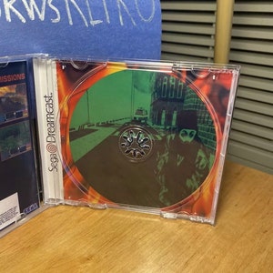 May include: A Sega Dreamcast game disc with a green and black image of a person in a black hooded jacket walking down a street. The disc is in a clear plastic case.