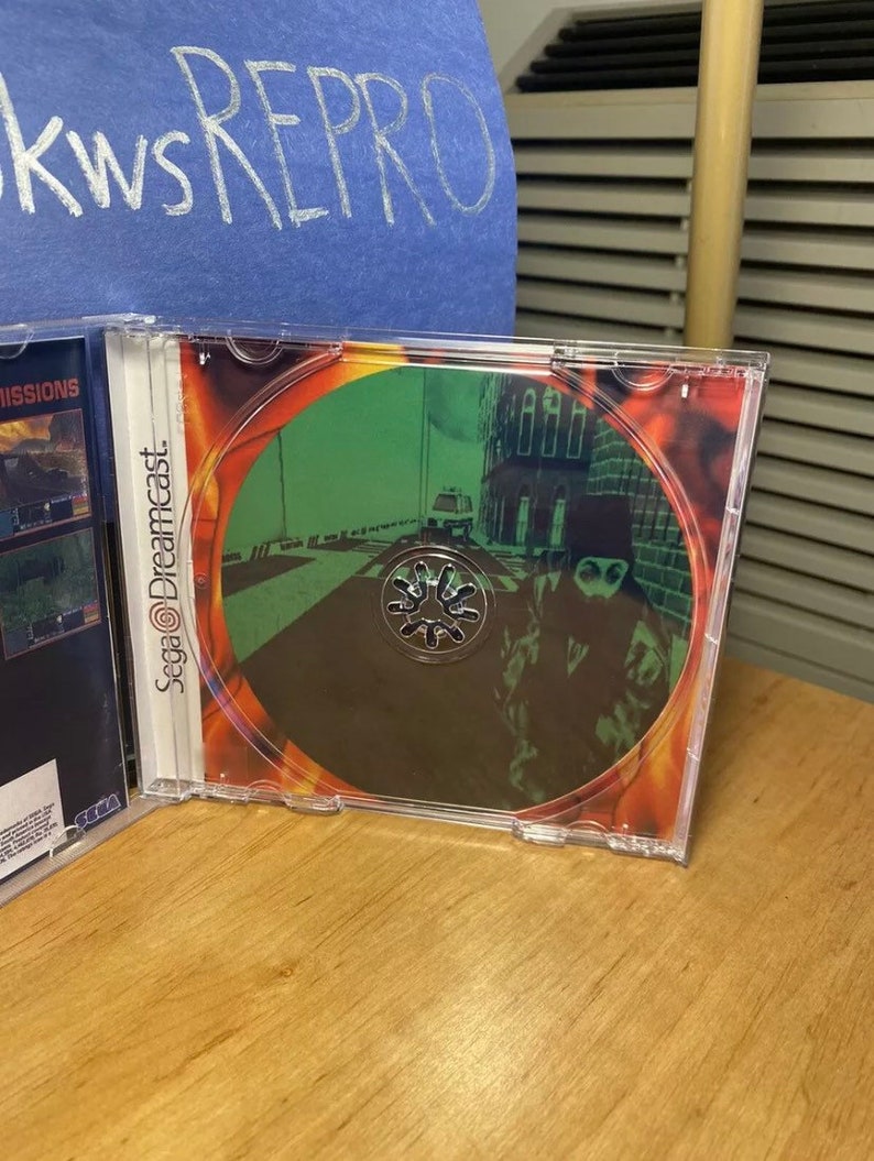 May include: A Sega Dreamcast game disc with a green and black image of a person in a black hooded jacket walking down a street. The disc is in a clear plastic case.
