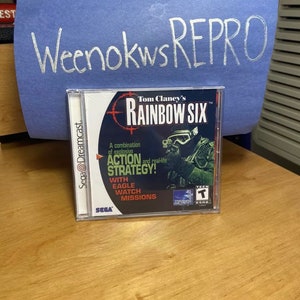 May include: A Sega Dreamcast game case for Tom Clancy's Rainbow Six. The case is green, black, and white with a picture of a soldier wearing a helmet and holding a gun. The text on the case reads "Tom Clancy's Rainbow Six" and "A combination of explosive action and real-life strategy!"