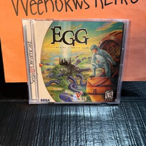 Może przedstawiać: Pudełko z grą Sega Dreamcast dla "EGG Elemental Gimmick Gear". Grafika na okładce przedstawia futurystyczny krajobraz z postacią w niebieskim kombinezonie, tytuł gry i ocenę ESRB.