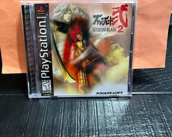 May include: A PlayStation game case for Bushido Blade 2. The cover art features a warrior with red hair and a sword. The game case is clear with the PlayStation logo on the side. The game is rated T for Teen.