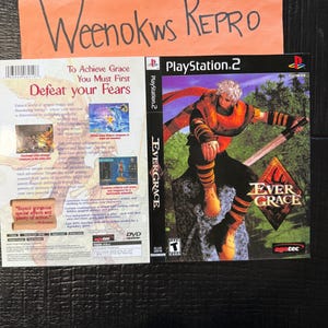Op de afbeelding: Een PlayStation 2 game case voor Evergrace. De cover toont een personage met wit haar, gekleed in oranje en zwarte bepantsering, met een zwaard. De titel van het spel staat in grote, gestileerde letters. De case ligt op een donkere ondergrond.