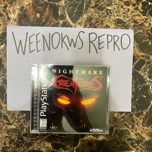 Peut inclure: Une boîte de jeu PlayStation pour Nightmare Creatures, un jeu classé pour adultes par Kalisto et Activision. La boîte présente un fond noir avec une créature rouge et noire aux yeux jaunes brillants.