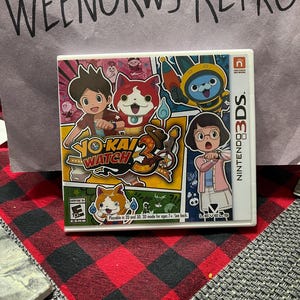 Könnte beinhalten: Eine Nintendo 3DS-Spielkassette für Yo-Kai Watch 3. Das Spielcover zeigt farbenfrohe Zeichentrickfiguren, darunter ein rot-weißes katzenartiges Wesen. Das Spiel ist für alle Altersgruppen freigegeben.