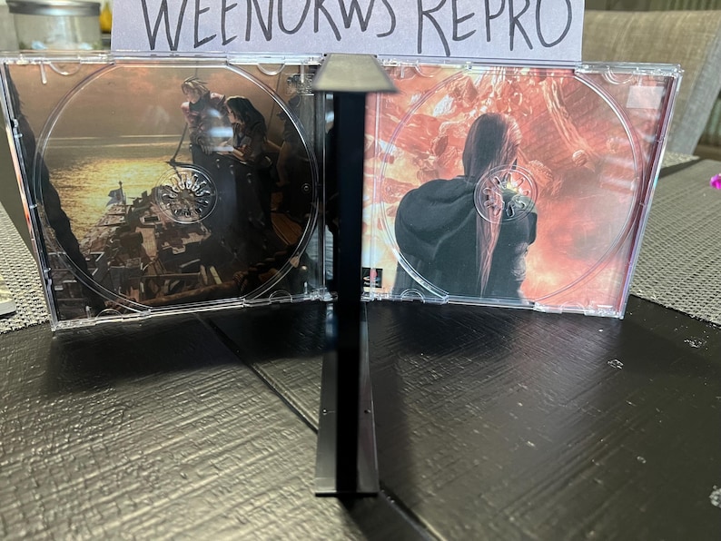 K&ouml;nnte beinhalten: Zwei transparente CD-H&uuml;llen aus Kunststoff mit schwarzen R&uuml;ckgraten, jede mit einer CD mit einem farbenfrohen Bild. Die linke CD zeigt ein dunkles Bild einer Person in einer dunklen Umgebung, w&auml;hrend die rechte CD ein helles Bild einer Person in einer feurigen Umgebung zeigt. Der Text "WEENORWS REPRO" ist auf einem wei&szlig;en Papier hinter den H&uuml;llen sichtbar.
