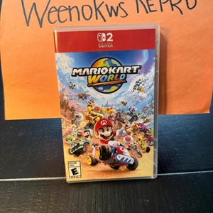 May include: A Nintendo Switch game case for Mario Kart World. The cover art shows Mario in a kart, surrounded by other characters and vehicles. The game case is in a clear plastic case with a red top.