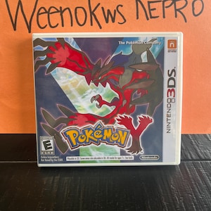 May include: A Nintendo 3DS game cartridge for Pokemon Y. The game features a red and black Pokemon on a blue and white background. The game is rated E for Everyone by the ESRB.