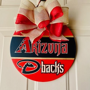 May include: A red, white, and black round wooden door hanger with the text "Arizona" and "Dbacks" and a red and white burlap bow.