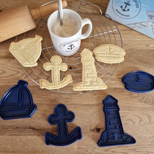 Könnte beinhalten: Ein Set an nautisch-thematischen Ausstechern, darunter ein Segelboot, ein Anker, ein Leuchtturm und eine Kapitänsmütze. Die Ausstecher sind aus blauem und weißem Kunststoff.