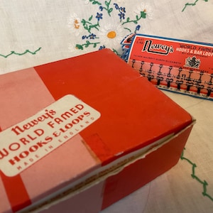 May include: Two vintage boxes of Newey's World Famed Hooks & Bar Loops are shown. One is red and pink with a label, the other is blue and red with text. Both boxes are made in England.