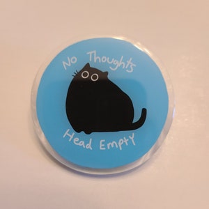 May include: A blue and white button with a black cat illustration and the text "No Thoughts Head Empty".