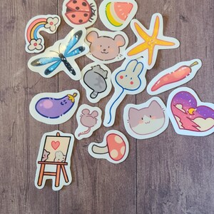 Op de afbeelding: Een verzameling kleurrijke stickers met verschillende schattige dier- en natuurontwerpen. De stickers bevatten een lieveheersbeestje, een watermeloen, een zeester, een vlinder, een muis, een konijn, een kat, een aubergine, een paddenstoel en een regenboog.