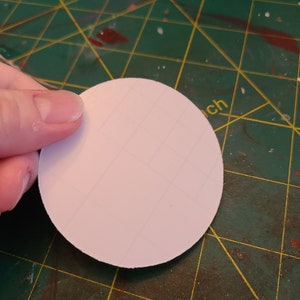 May include: A white, round, blank sticker on a green cutting mat.