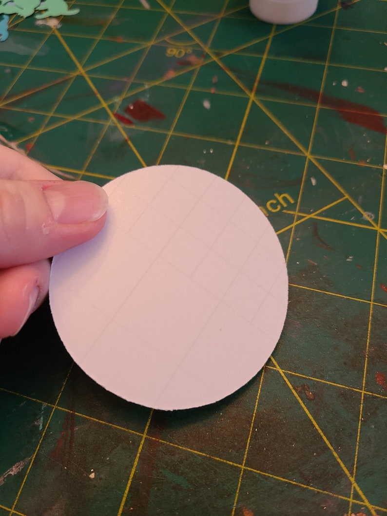 May include: A white, round, blank sticker on a green cutting mat.