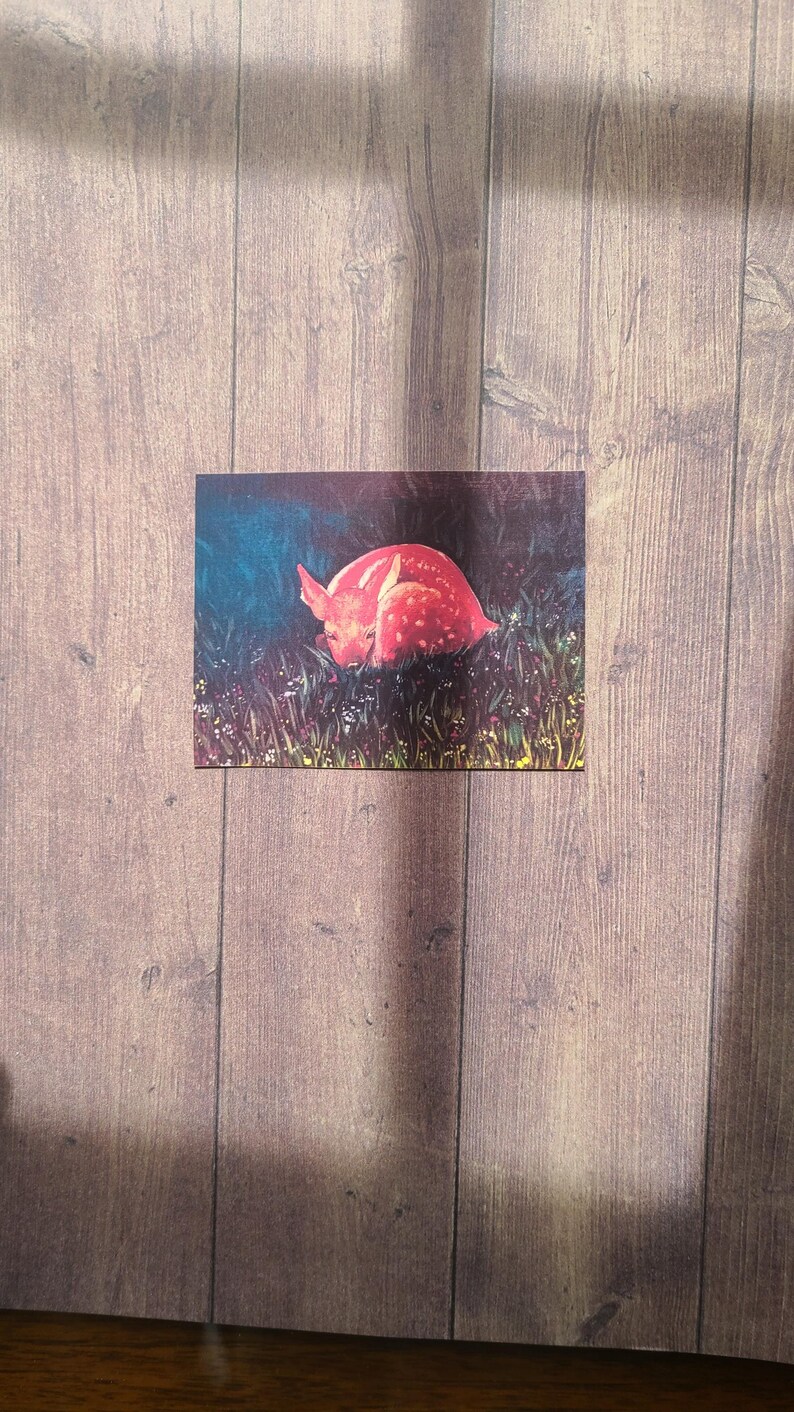 May include: A pink and white spotted fawn lying down in a field of green grass and white flowers.